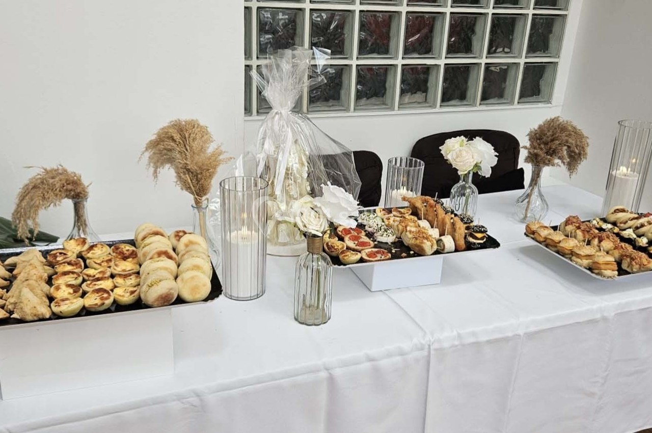 Plateaux de viennoiseries et amuse-bouches disposés sur une table blanche décorée de fleurs et bougies.