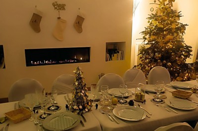 Table de fête décorée avec vaisselle élégante, sapin de Noël illuminé et cheminée allumée en arrière-plan.