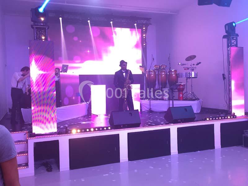 Un musicien joue du saxophone sur une scène éclairée par des lumières violettes, avec des instruments en arrière-plan.