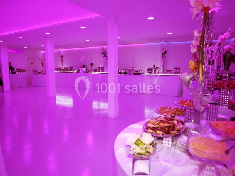 Salle de réception éclairée en rose avec des tables garnies de plats et un buffet en arrière-plan.