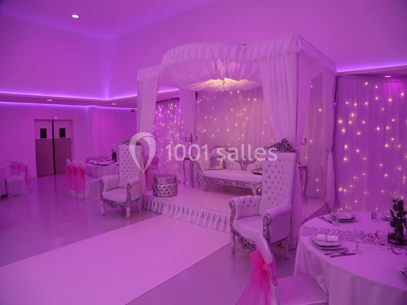 Salle de réception décorée en rose et blanc avec un lit à baldaquin, chaises élégantes et éclairage tamisé.