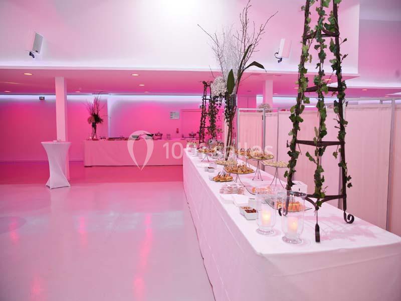 Salle de réception décorée avec des tables de buffet garnies de plats et de bougies, éclairage rose tamisé.