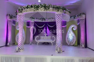 Mains d'un couple portant des alliances, posées sur un bouquet de fleurs blanches et violettes.