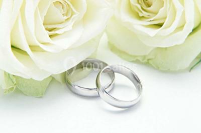 Mains d'un couple portant des alliances, posées sur un bouquet de fleurs blanches et violettes.