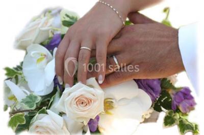 Mains d'un couple portant des alliances, posées sur un bouquet de fleurs blanches et violettes.