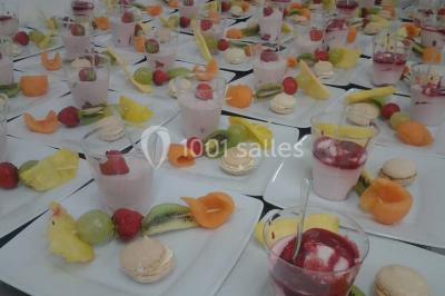 Assortiment de desserts avec verrines, fruits frais, macarons et coulis, disposés sur des assiettes blanches.