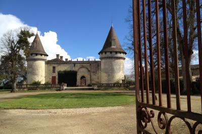 Château en pierre éclairé à la tombée de la nuit, entouré d'arbres et surmonté d'un ciel nuageux.