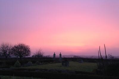 Château en pierre éclairé à la tombée de la nuit, entouré d'arbres et surmonté d'un ciel nuageux.