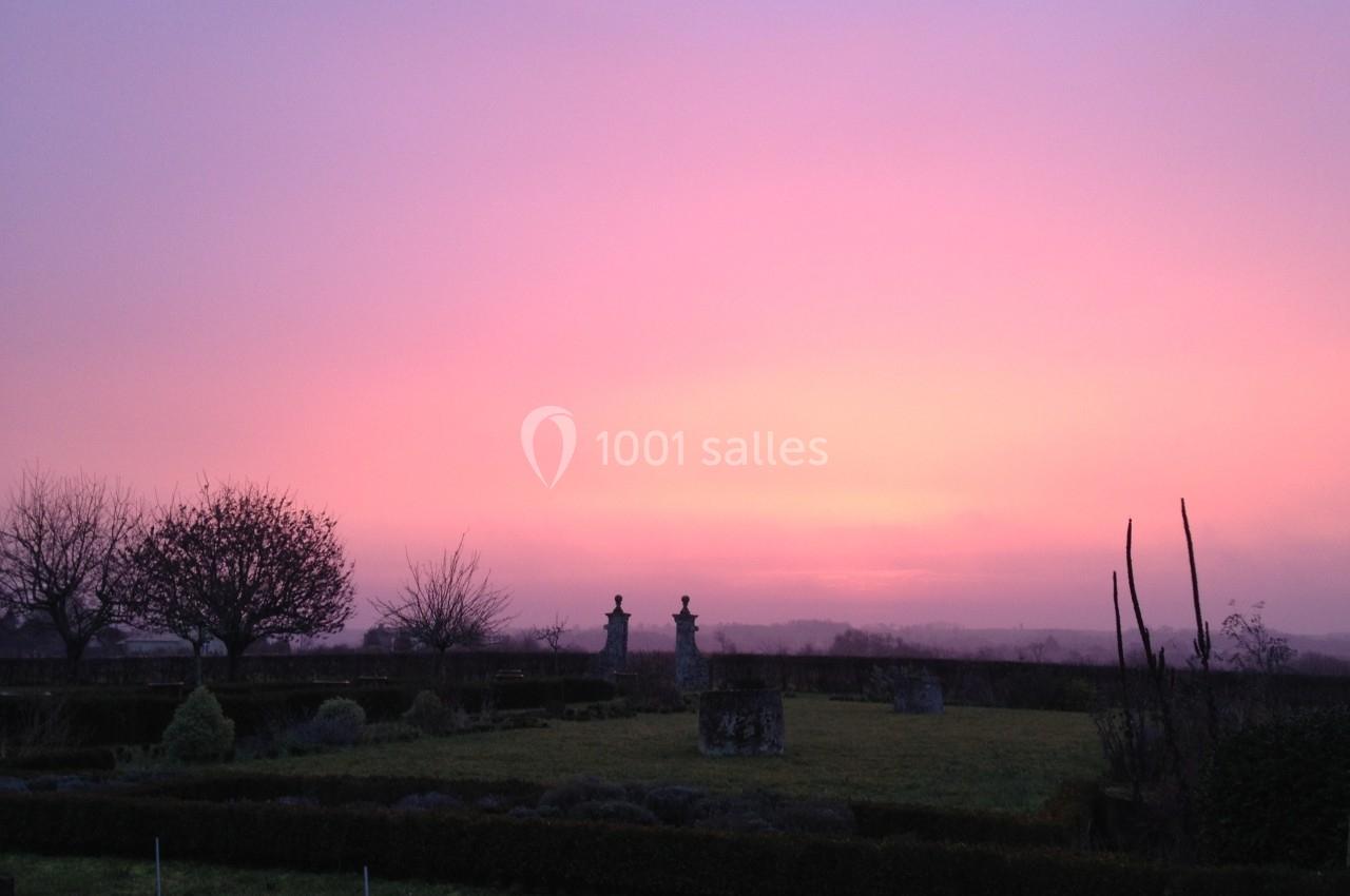 Ciel rose au coucher du soleil sur un jardin avec arbres dénudés, statues et haies en hiver.