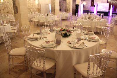 Château en pierre éclairé à la tombée de la nuit, entouré d'arbres et surmonté d'un ciel nuageux.