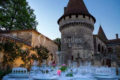 Château en pierre éclairé à la tombée de la nuit, entouré d'arbres et surmonté d'un ciel nuageux.