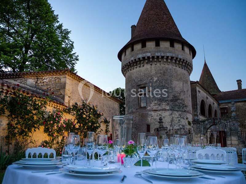 Table dressée pour un repas en extérieur devant un château ancien avec tours et murs en pierre au crépuscule.