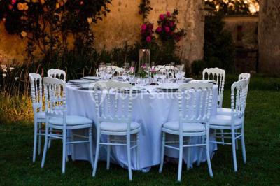 Château en pierre éclairé à la tombée de la nuit, entouré d'arbres et surmonté d'un ciel nuageux.