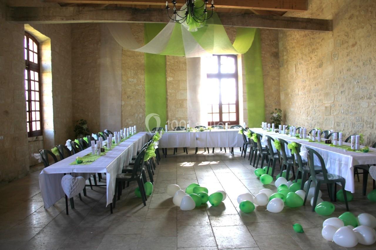 Salle décorée pour un événement avec des tables en U, nappes blanches, chaises vertes et ballons verts et blancs au sol.