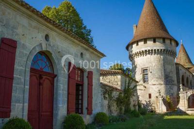 Château en pierre éclairé à la tombée de la nuit, entouré d'arbres et surmonté d'un ciel nuageux.