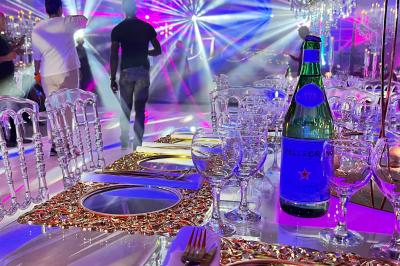 Voiture de sport verte aux portes papillon ouvertes, entourée de fumée et d'une foule dans un lieu éclairé.