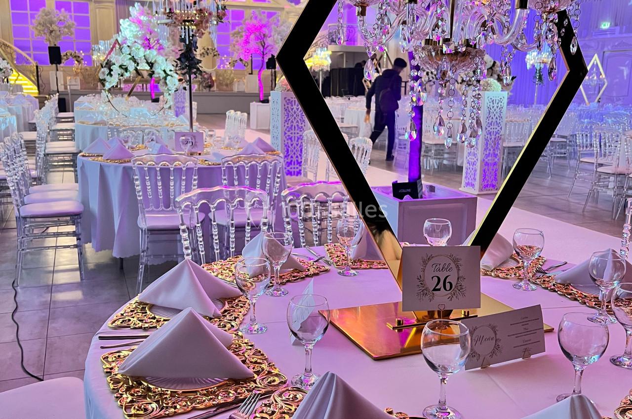 Salle de réception décorée avec des tables élégantes, nappes blanches, chandeliers et éclairage rose.