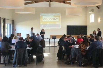 Chambre avec lit double, parquet en bois, table de chevet, lampe, chaise verte et banc au pied du lit.