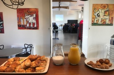 Chambre avec lit double, parquet en bois, table de chevet, lampe, chaise verte et banc au pied du lit.