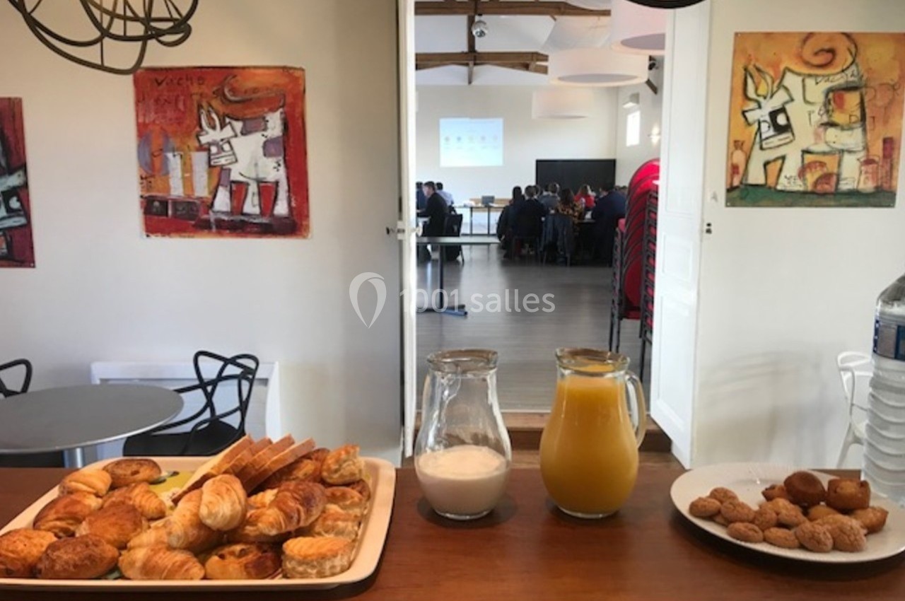 Plateau de viennoiseries, carafe de jus d'orange, lait et biscuits disposés sur un comptoir dans une salle de réunion.