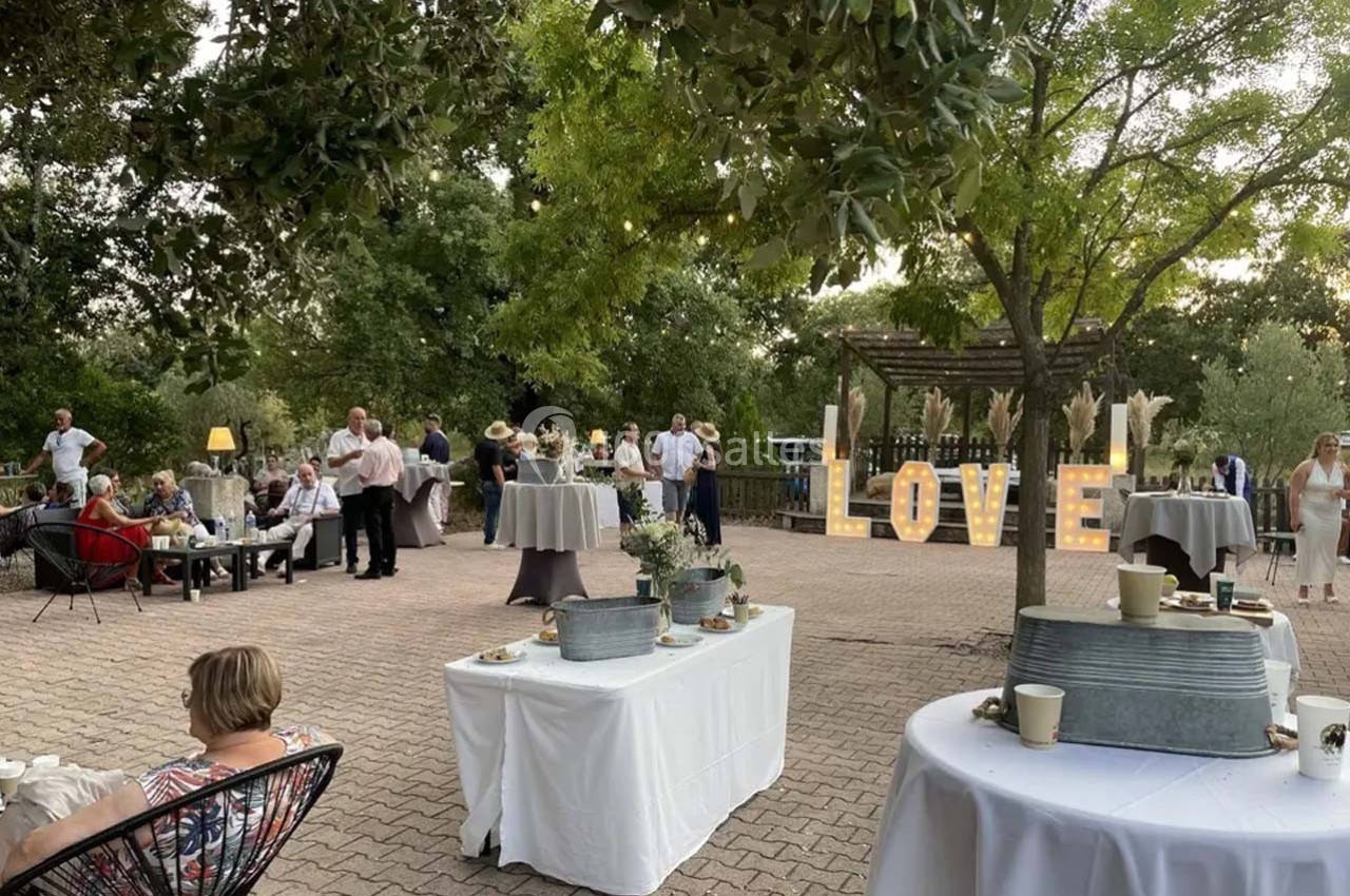 Groupe de personnes réunies dans un jardin pour un événement, avec des tables dressées et des lettres lumineuses ’LOVE’.