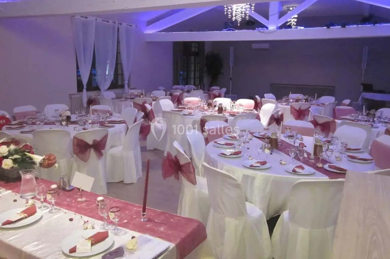 Salle de réception décorée avec des tables rondes, nappes blanches, chemins de table roses et chaises assorties.
