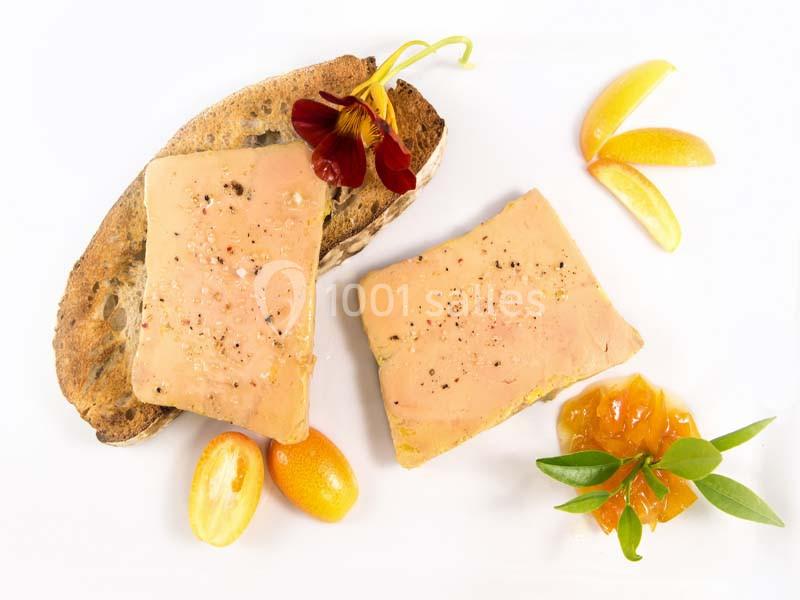 Deux tranches de foie gras sur une assiette avec pain grillé, confiture, kumquat et décoration florale.