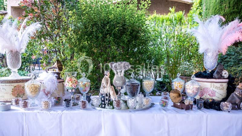 Table décorée avec des vases remplis de bonbons, plumes blanches et éléments décoratifs dans un jardin verdoyant.