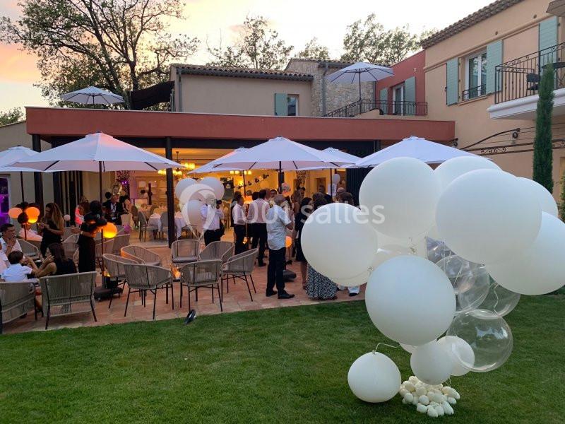 Groupe de personnes réunies dans une cour extérieure au coucher du soleil, entourées de ballons blancs et de parasols.