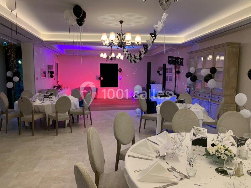 Salle de réception décorée avec des ballons noirs et blancs, tables dressées et éclairage coloré sur une scène.