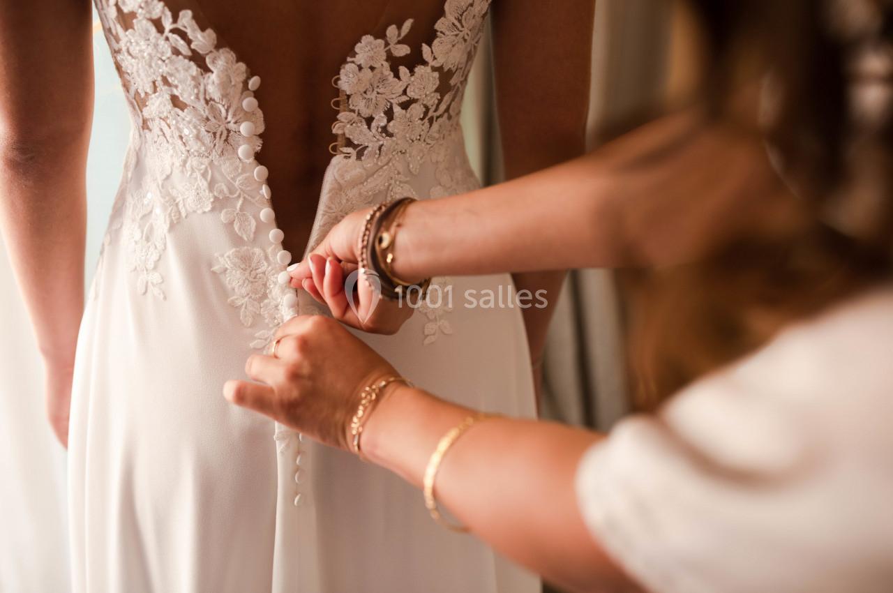Une personne ferme les boutons du dos d'une robe de mariée ornée de dentelle.