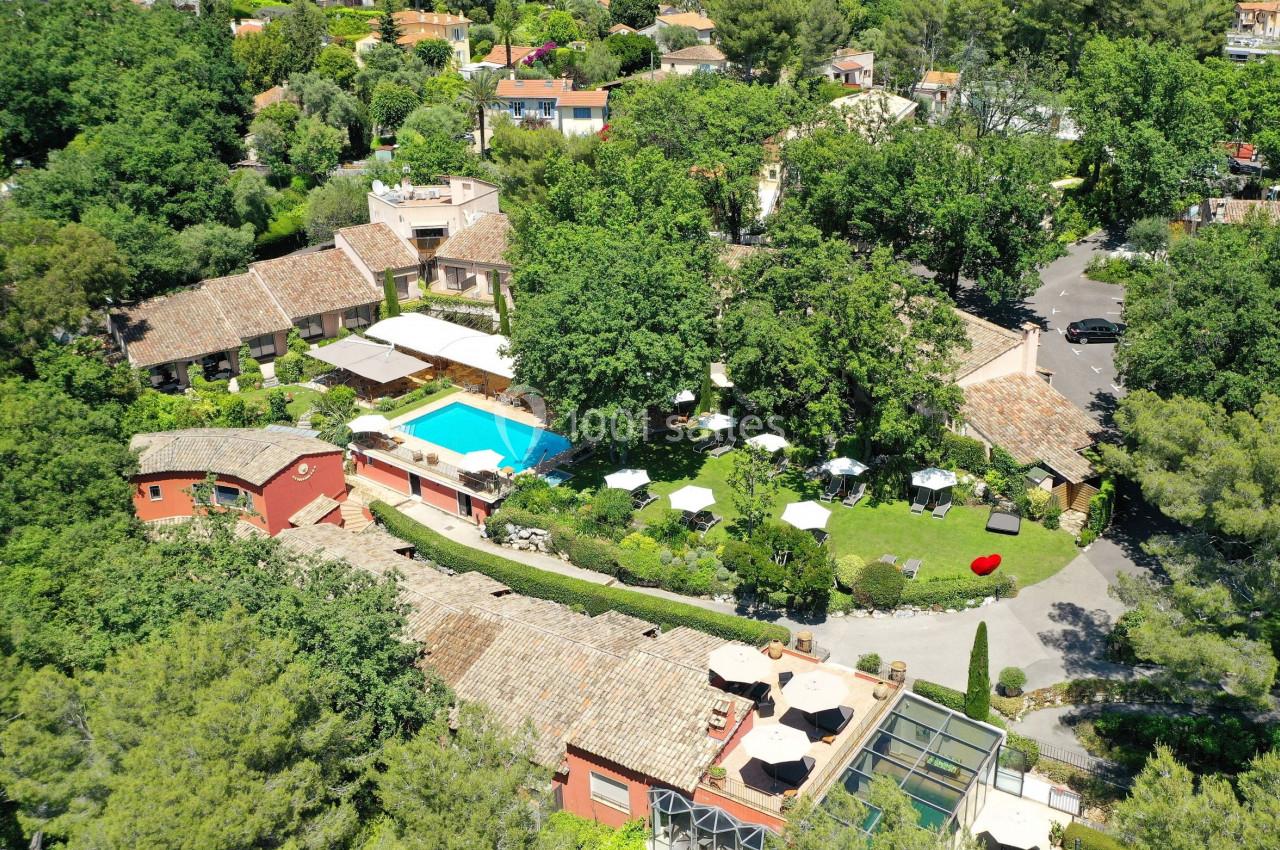 Vue aérienne d'un domaine avec piscine, bâtiments aux toits en tuiles, jardins verdoyants et terrasses aménagées.