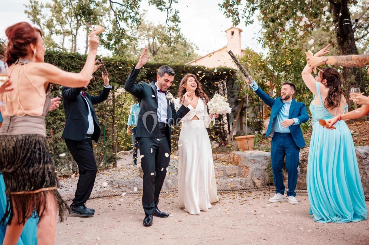Un couple de mariés souriant entouré d'invités lançant des pétales dans un jardin en plein air.