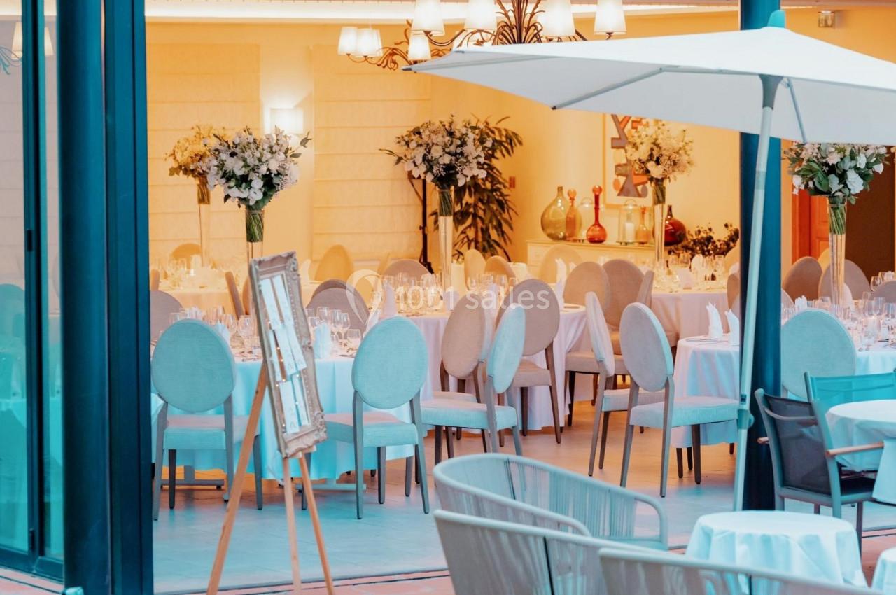 Salle de réception élégante avec tables dressées, chaises claires, décor floral et lumière chaleureuse.