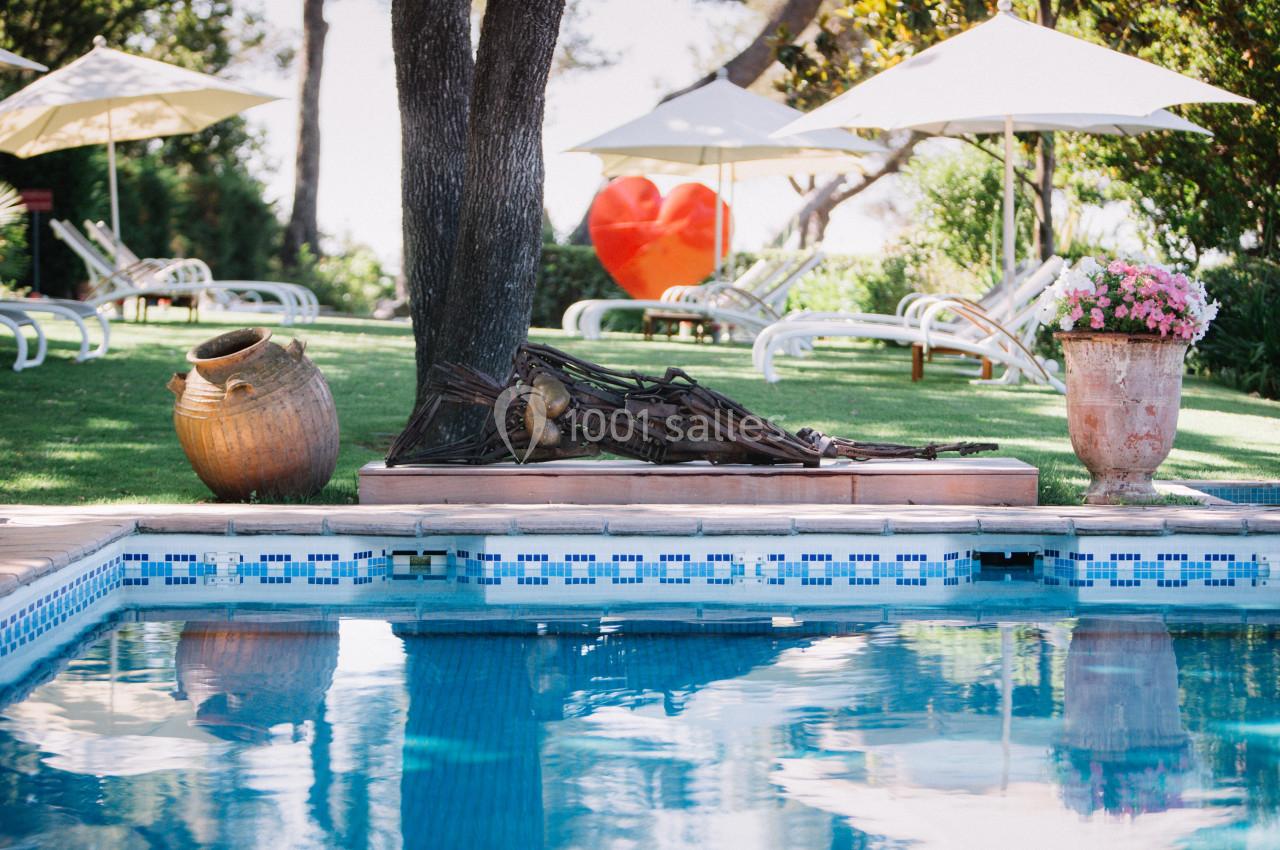 Chaises longues et parasols sur une pelouse près d'une piscine, avec des jarres et des fleurs en décoration.
