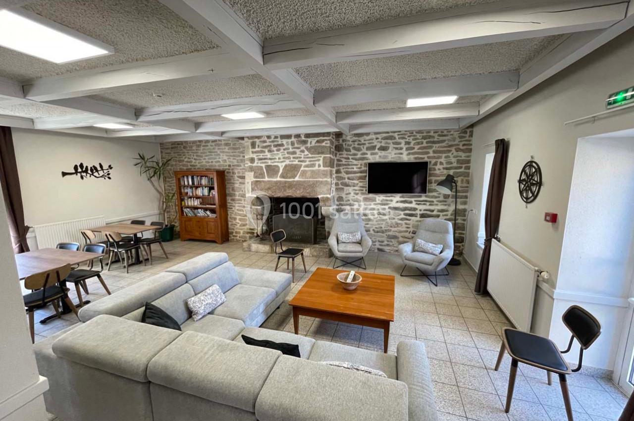 Location salle Plouay (Morbihan) - Domaine de Manehouarn #7 Salon spacieux avec canapé gris, table basse en bois, cheminée en pierre, télé murale et coin repas adjacent.