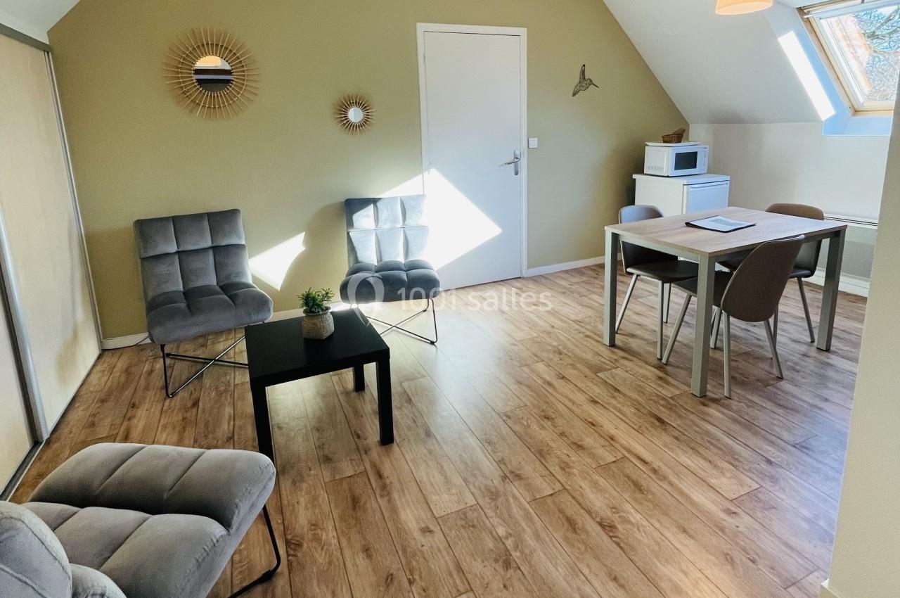 Location salle Plouay (Morbihan) - Domaine de Manehouarn #13 Salon lumineux avec parquet, fauteuils gris, table à manger, micro-ondes et décoration murale, sous une lumière naturelle.