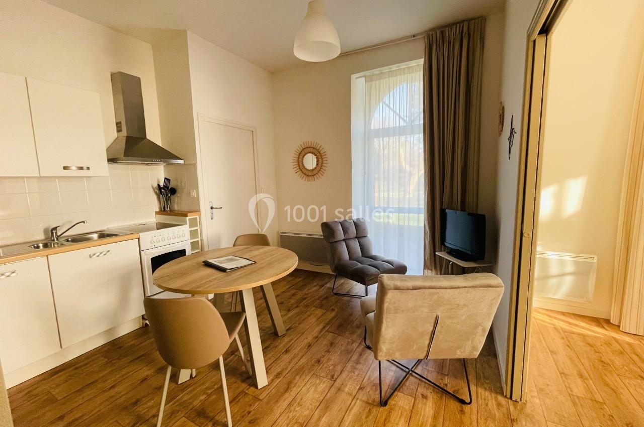 Location salle Plouay (Morbihan) - Domaine de Manehouarn #14 Cuisine ouverte avec table ronde, chaises, fauteuils, téléviseur, et grande fenêtre laissant entrer la lumière naturelle.