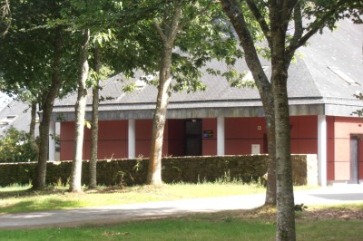 Cuisine ouverte avec table ronde, chaises, fauteuils, téléviseur, et grande fenêtre laissant entrer la lumière naturelle.