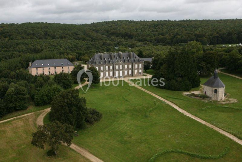 Vue aérienne d'un domaine avec un château, une chapelle, des bâtiments annexes et un parc entouré de forêt.