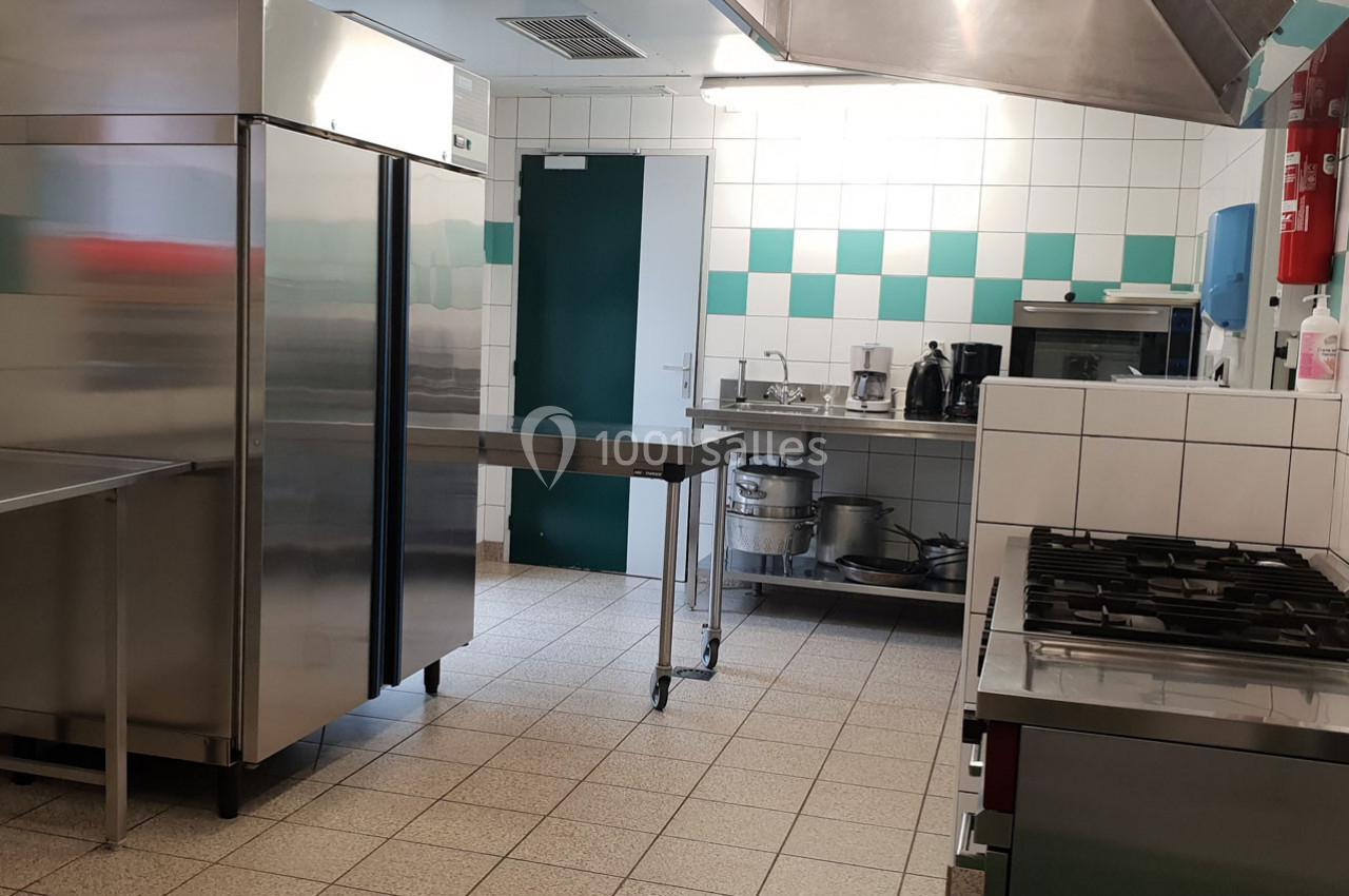 Cuisine professionnelle équipée avec réfrigérateur, plan de travail en inox, évier, plaques de cuisson et carrelage mural.