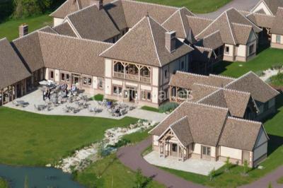 Paysage automnal avec un lac reflétant des arbres aux feuilles rouges et orangées sous un ciel nuageux.