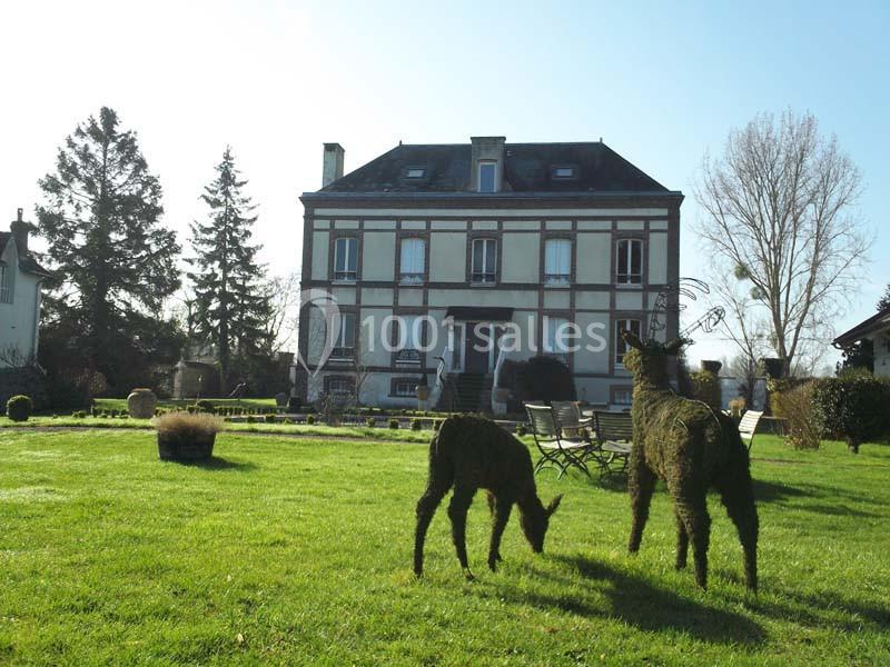 Deux sculptures végétales en forme de cerfs sur une pelouse devant une grande maison en briques et colombages.