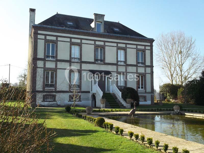 Façade d'une maison en briques avec un escalier central, entourée d'un jardin et d'un bassin rectangulaire.