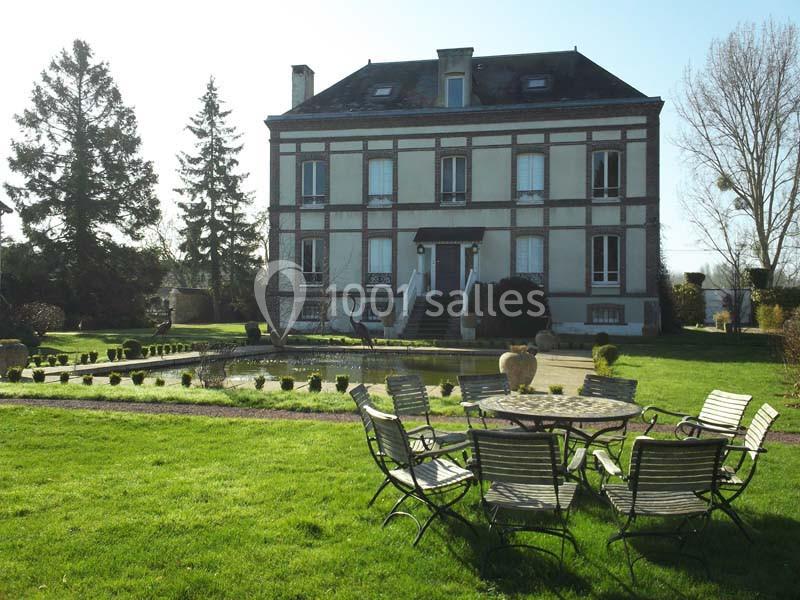 Maison ancienne en briques avec un jardin, une fontaine et des chaises disposées autour d'une table sur la pelouse.