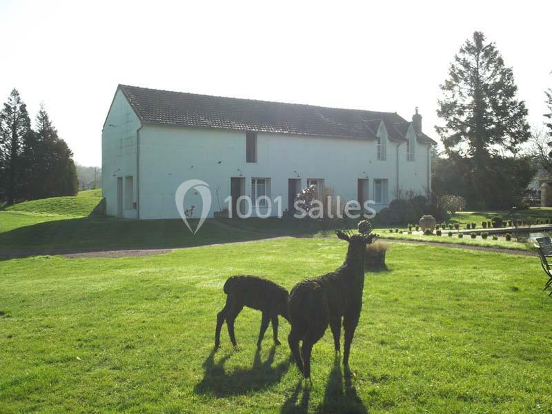 Deux sculptures d'animaux en buis sur une pelouse devant une grande maison blanche à la campagne.