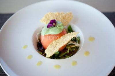 Paysage automnal avec un lac reflétant des arbres aux feuilles rouges et orangées sous un ciel nuageux.