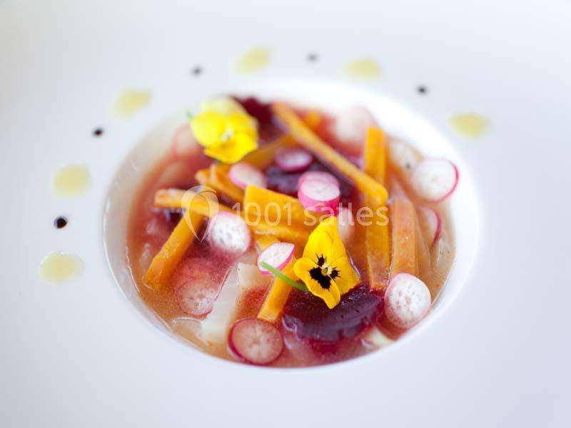 Assiette gastronomique avec légumes colorés, fleurs comestibles et sauce présentée de manière artistique.