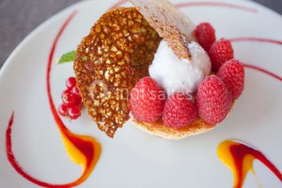 Paysage automnal avec un lac reflétant des arbres aux feuilles rouges et orangées sous un ciel nuageux.