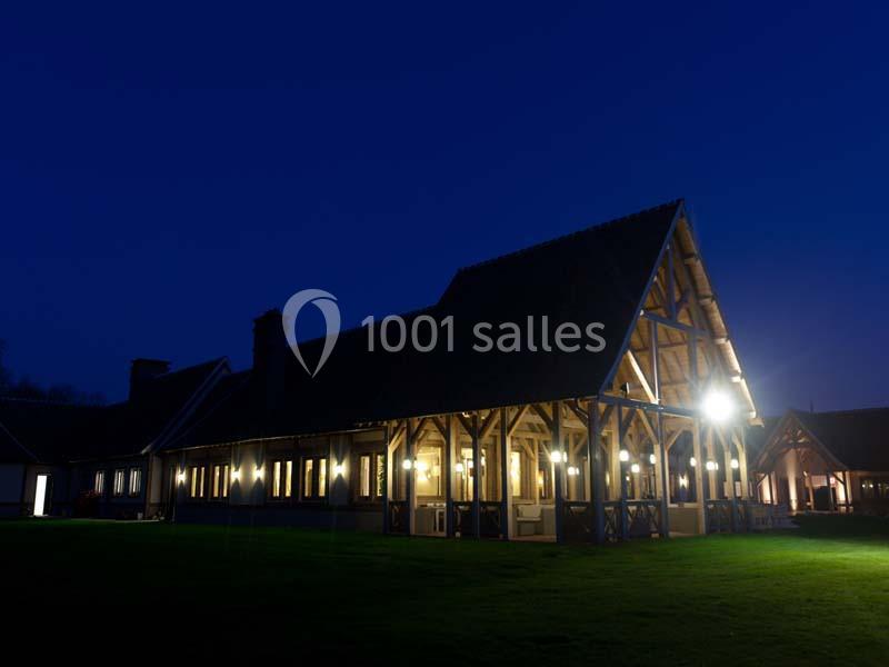 Bâtiment à ossature bois éclairé la nuit, entouré d'une pelouse sombre sous un ciel bleu foncé.